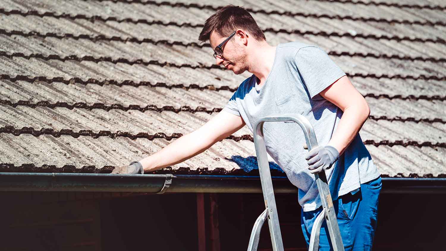 Young man on a ladder cleaning house gutter