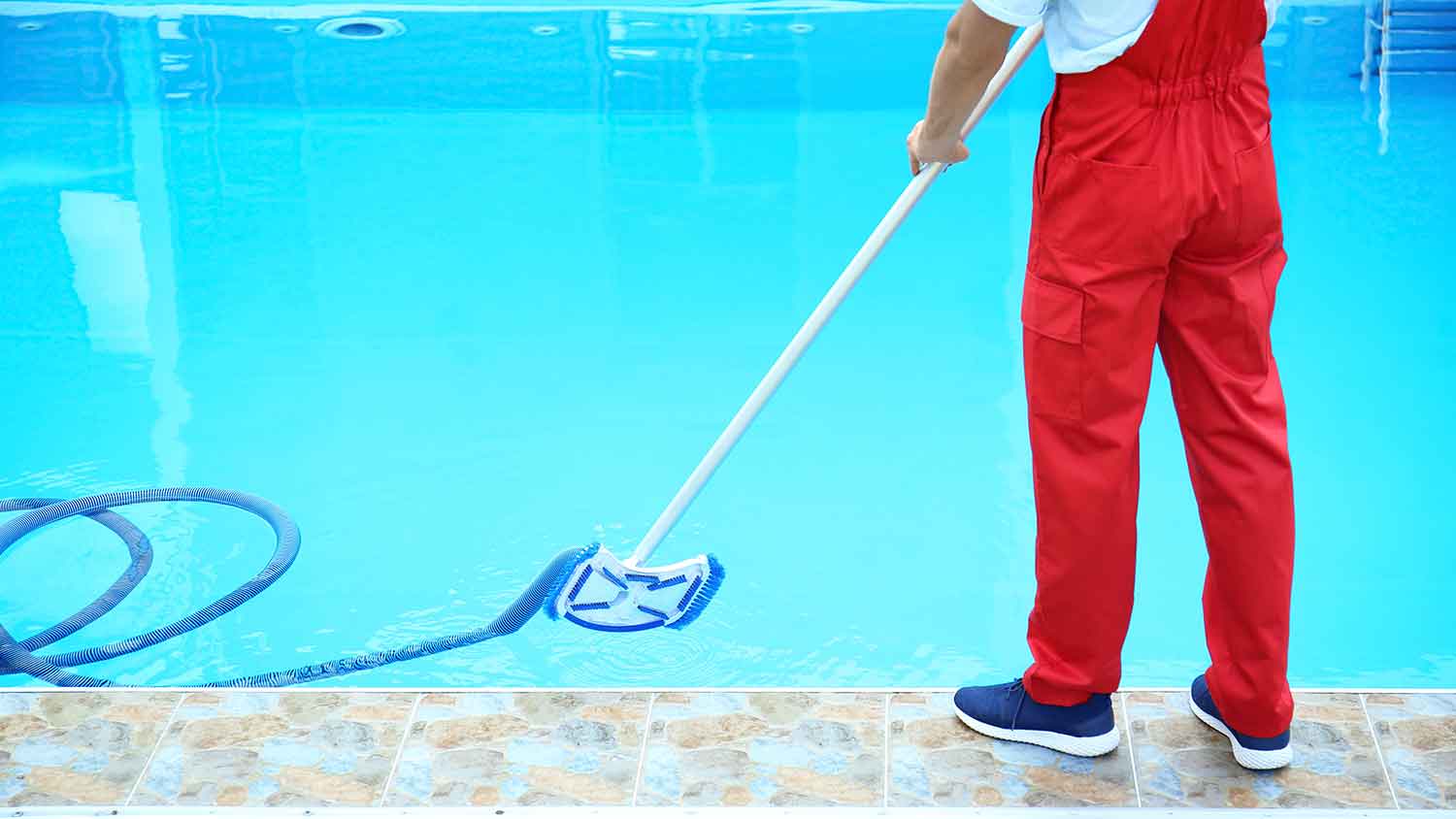 Worker using pool vacuum to clean swimming pool