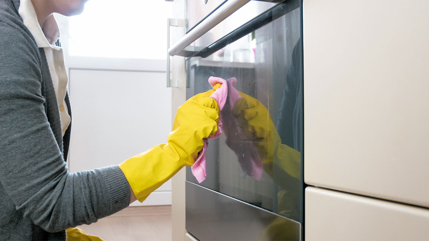 A person cleans the outside of oven glass