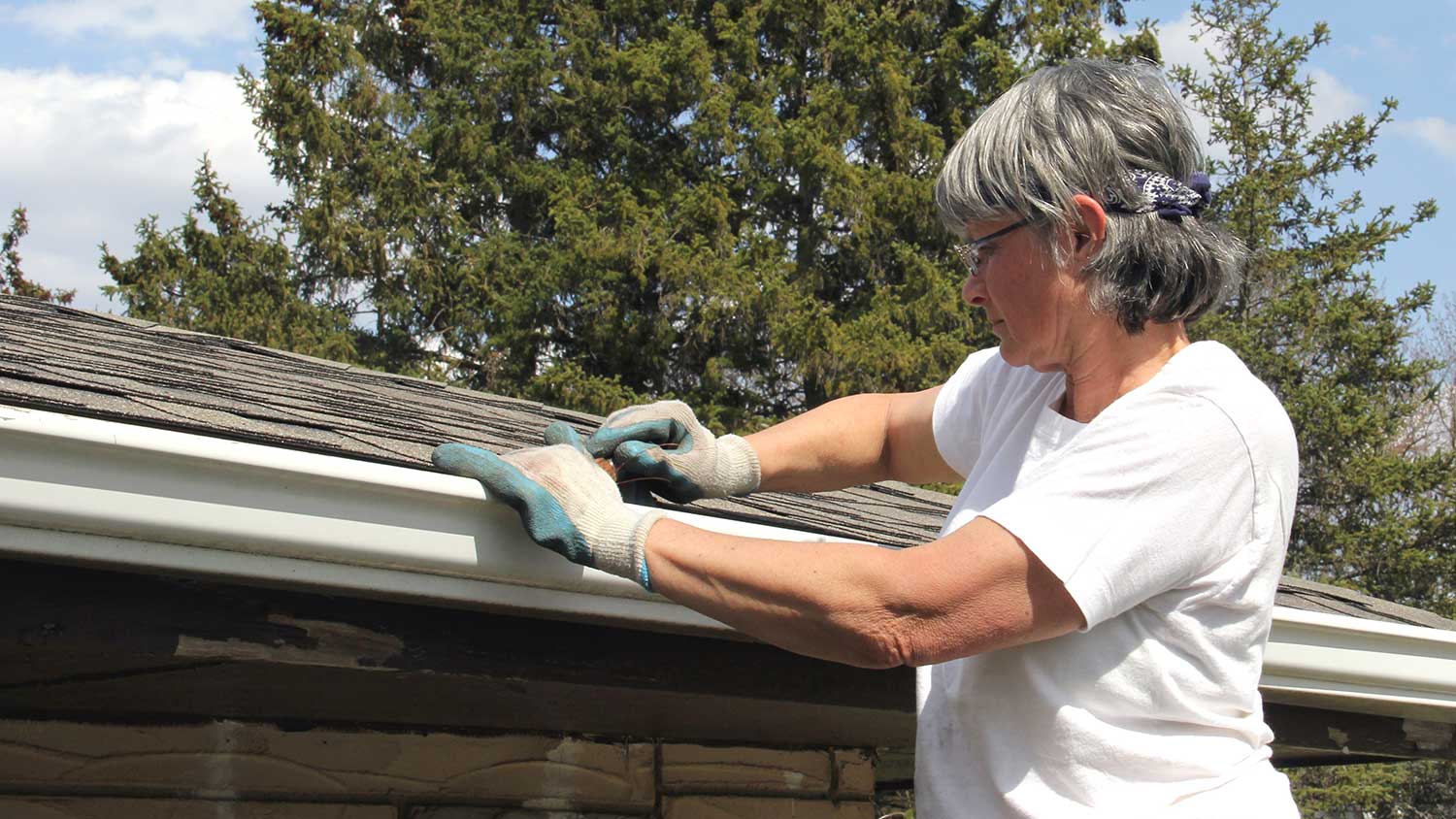 Woman standing on ladder cleaning rain gutters