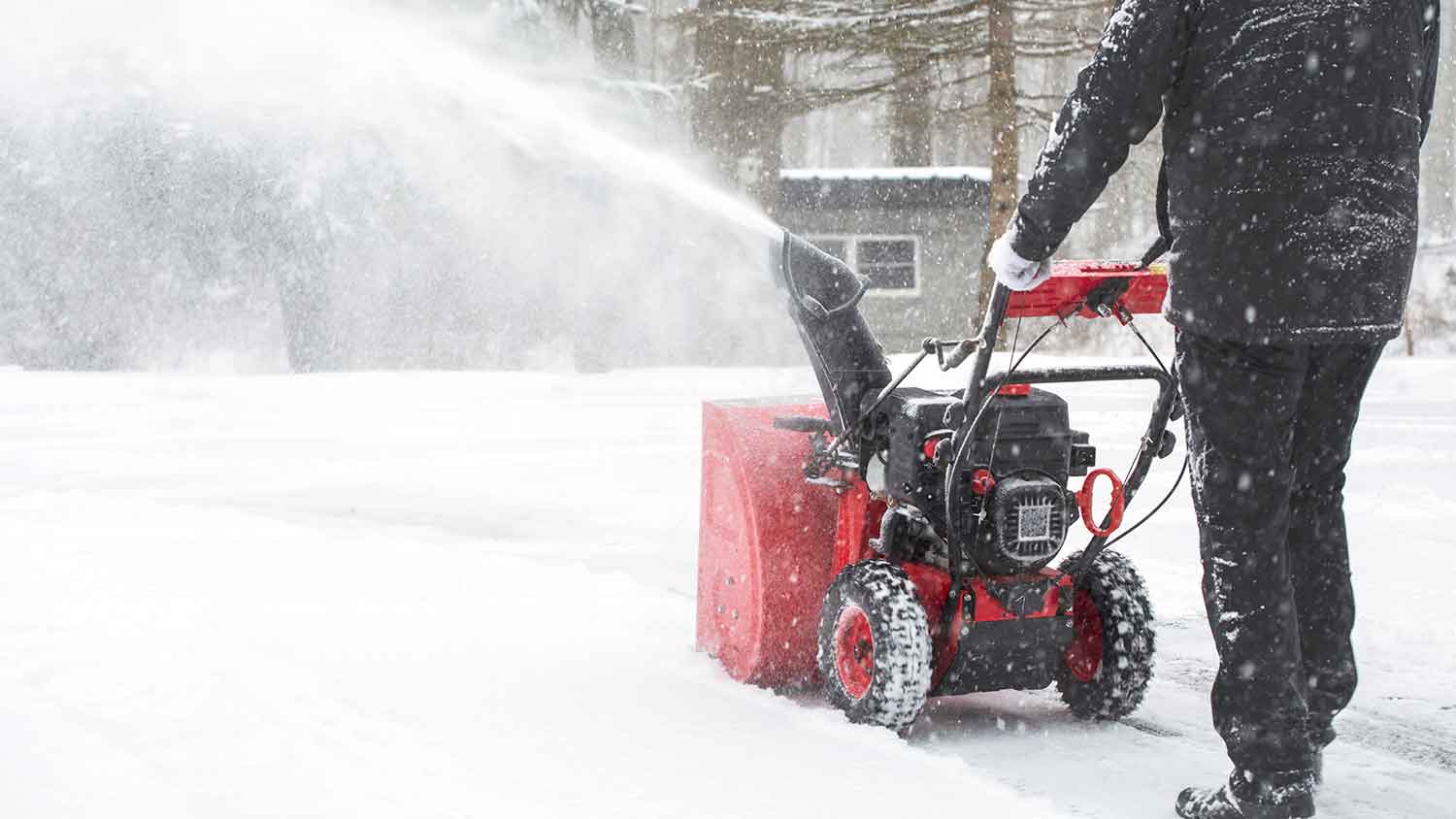 Man using snow blower to clear snow outside of a cabin