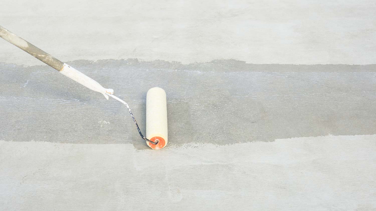 Close-up of a person applying sealer to a concrete surface with a roller