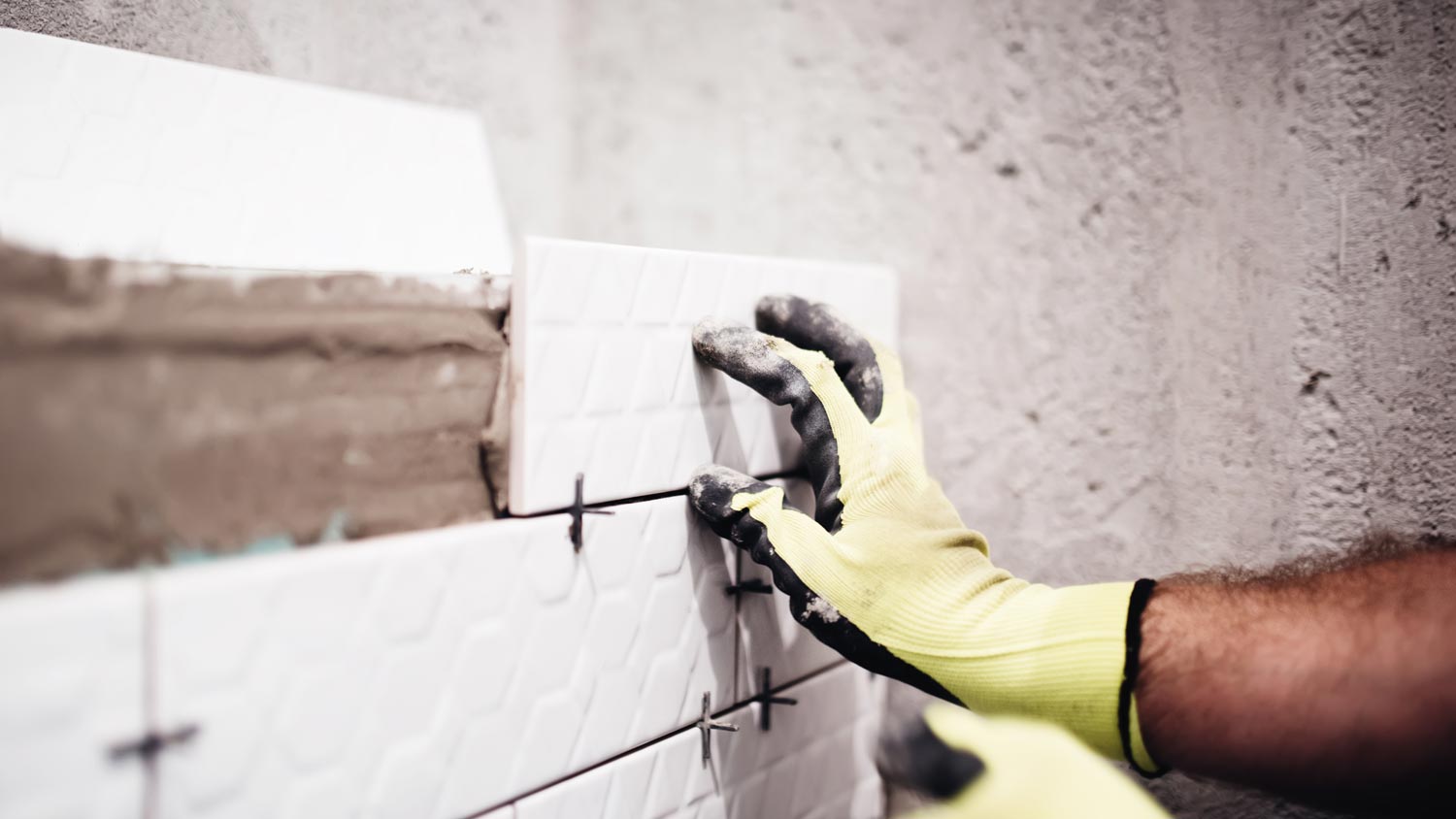 Close-up of a man’s hand putting tiles on wall