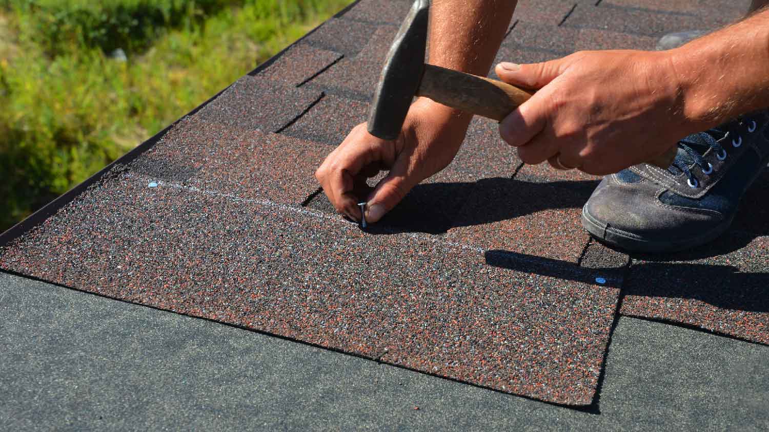 Close-up of a person installing shingles on asphalt underlayment