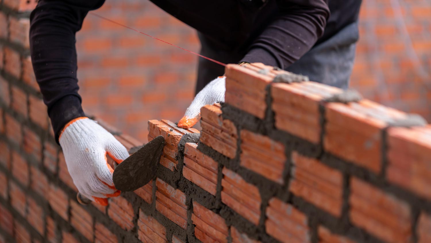 A construction building a wall by laying bricks and mortar