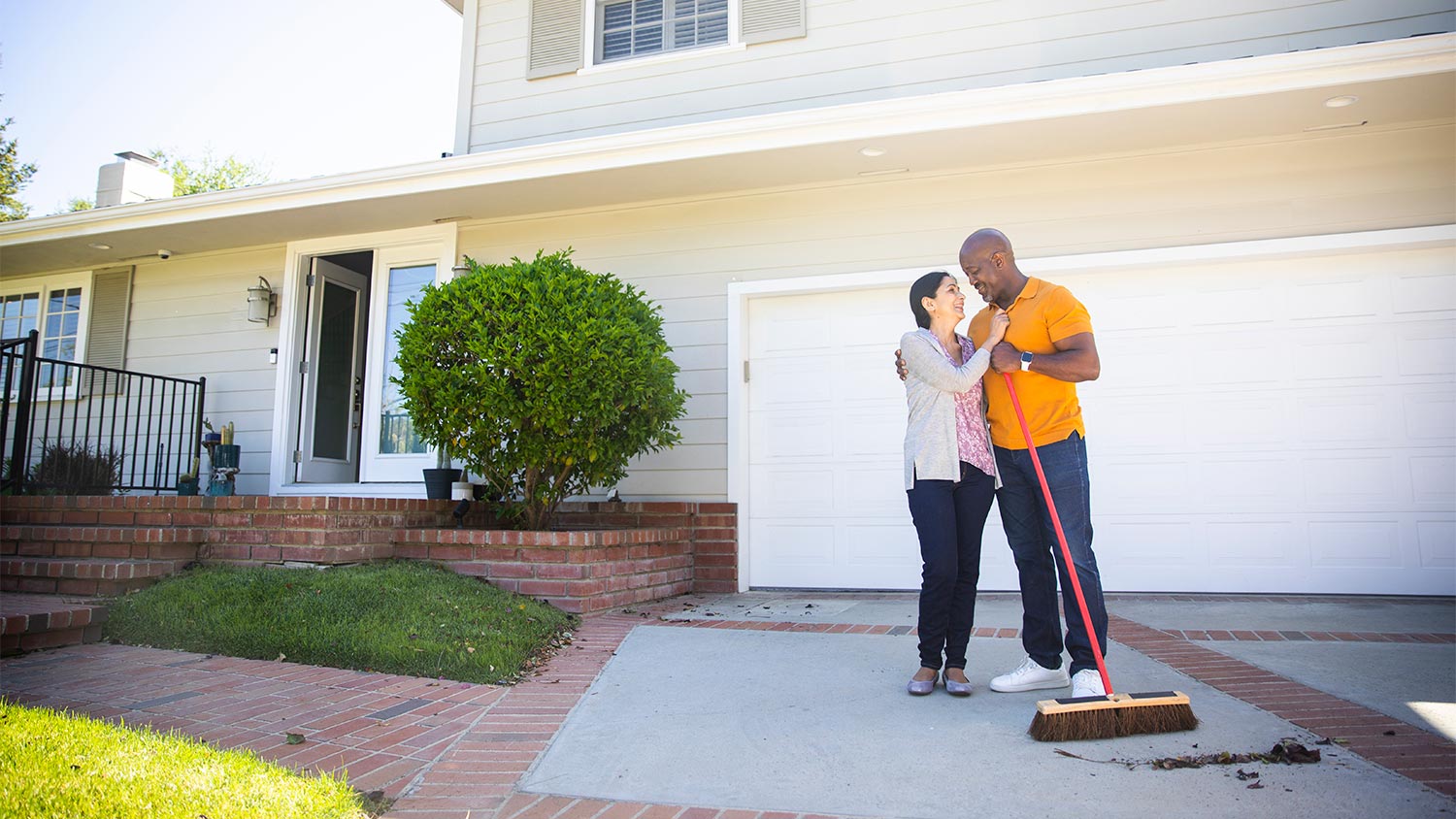 Couple sweeping driveway in front yard.