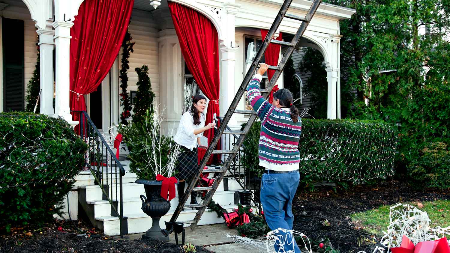 Couple setting up ladder to hang Christmas lights