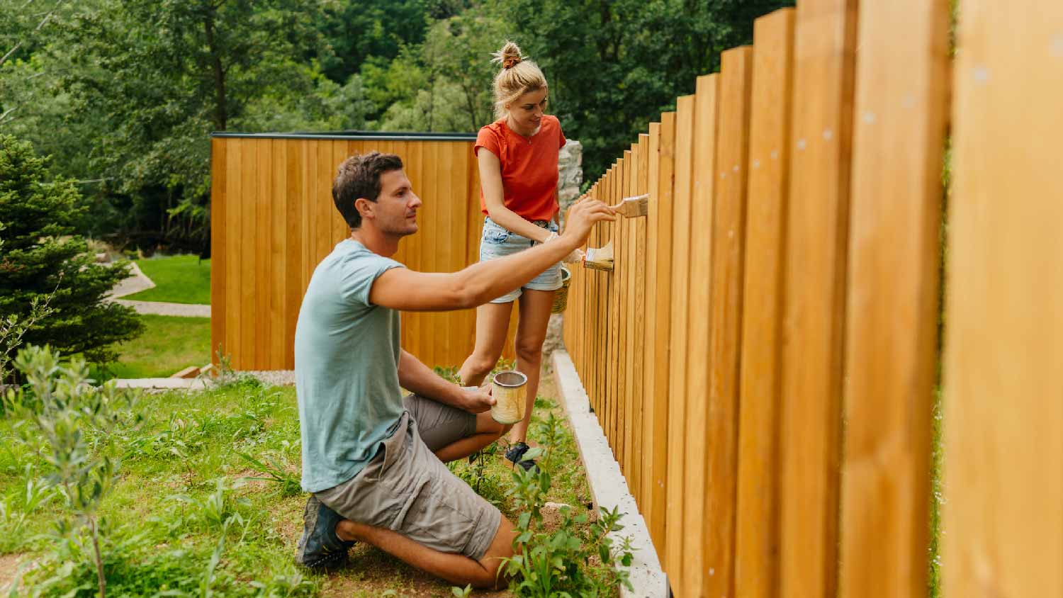 A couple staining a wooden fence