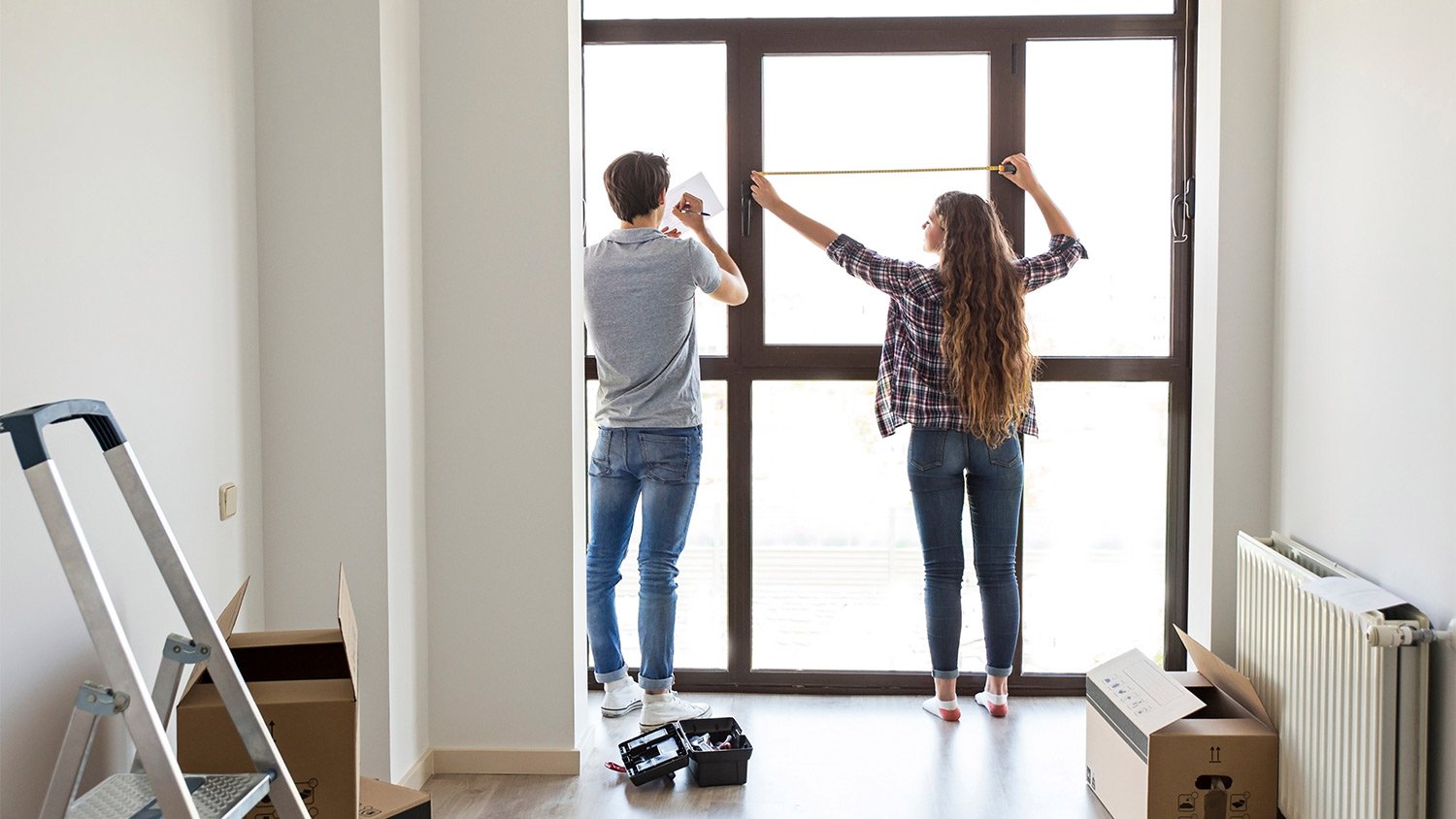 Young male and female measuring window in apartment.