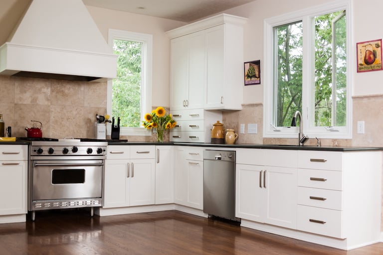 a modern home kitchen with dark wood floors, white cabinets, silver appliances, and tan tiled walls