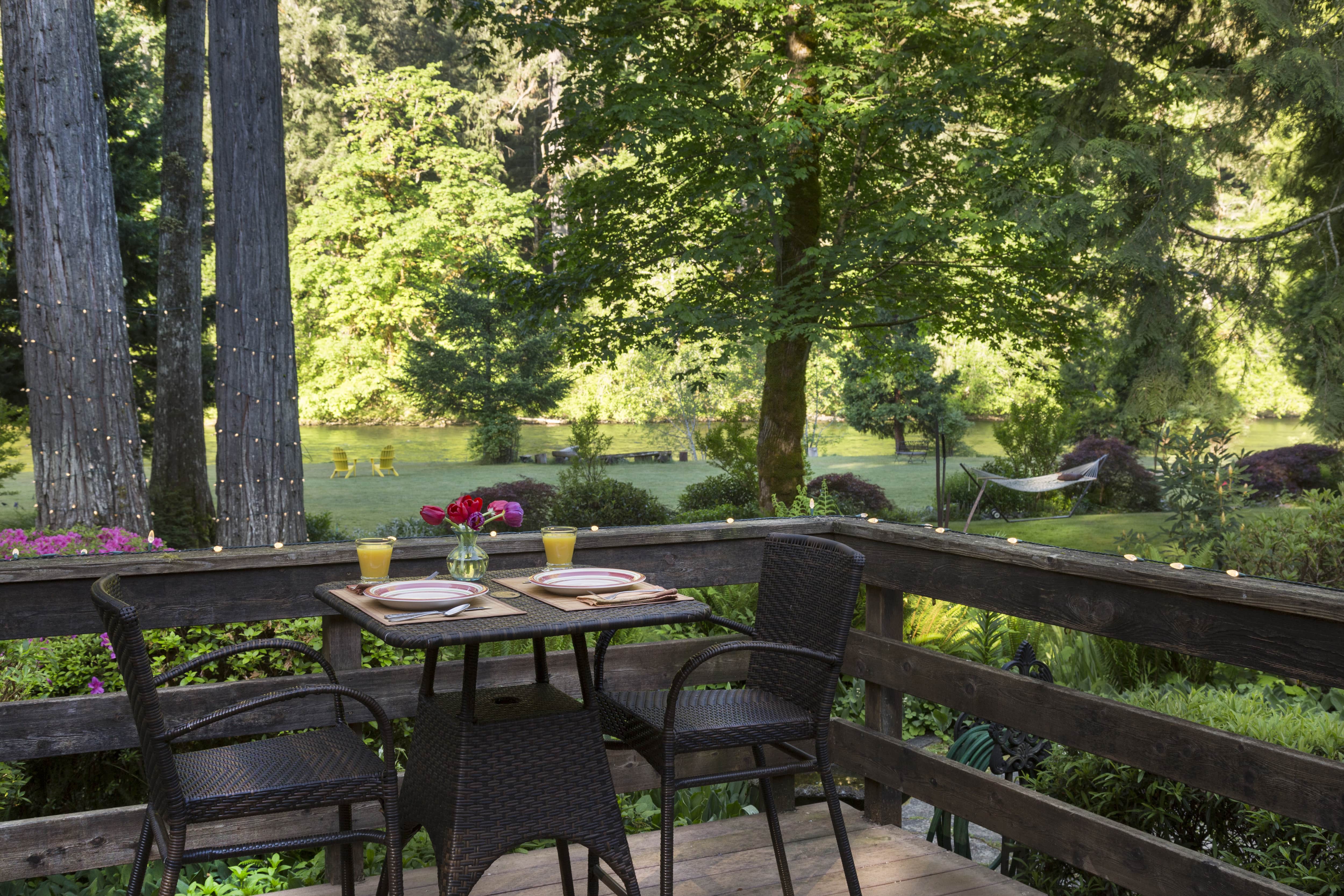 Patio with black table and chairs and horizontal wood railings overlooking a lawn and lake