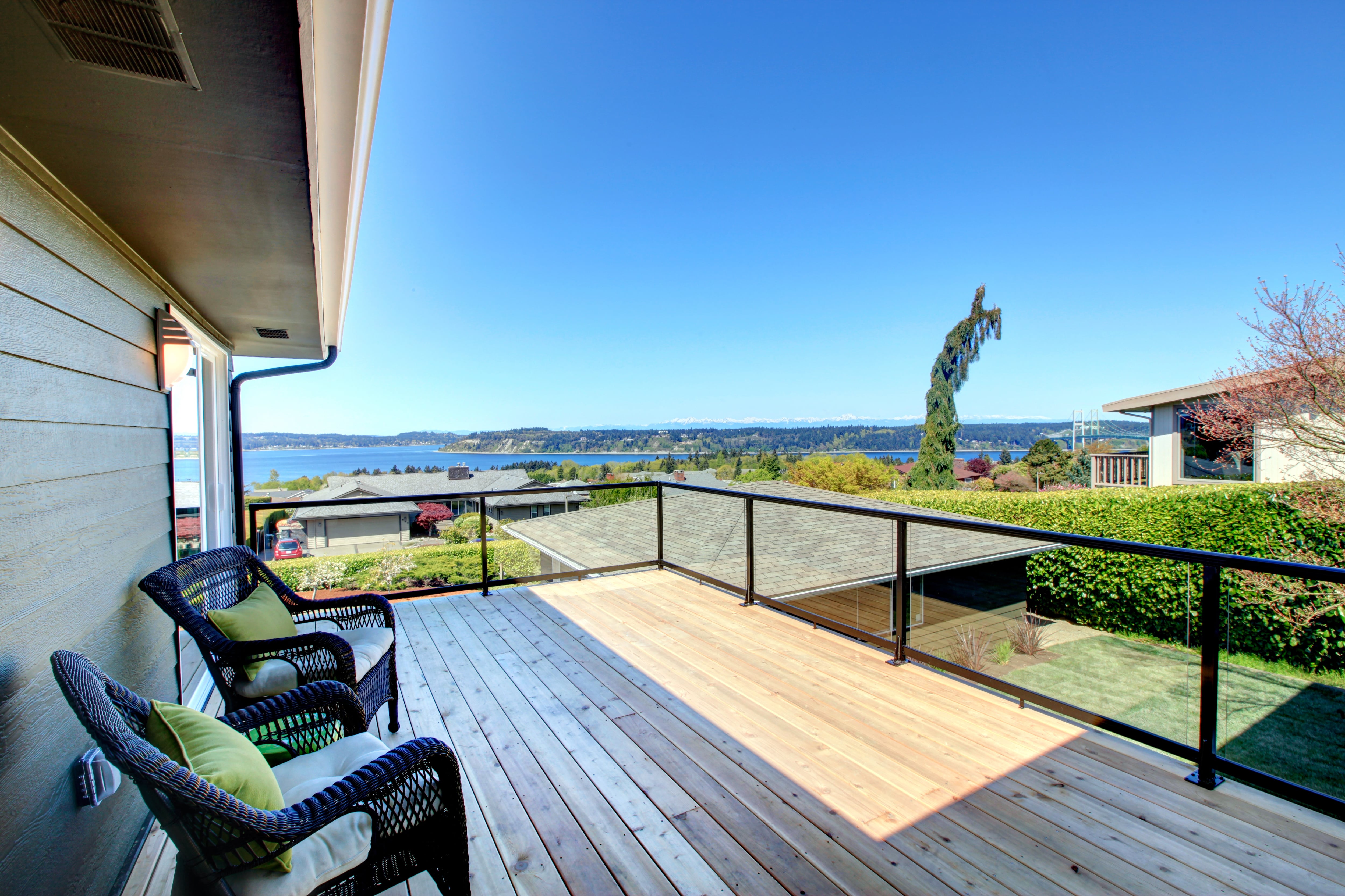 Small walkout patio with plexiglass railings and black wicker chairs overlooking backyard