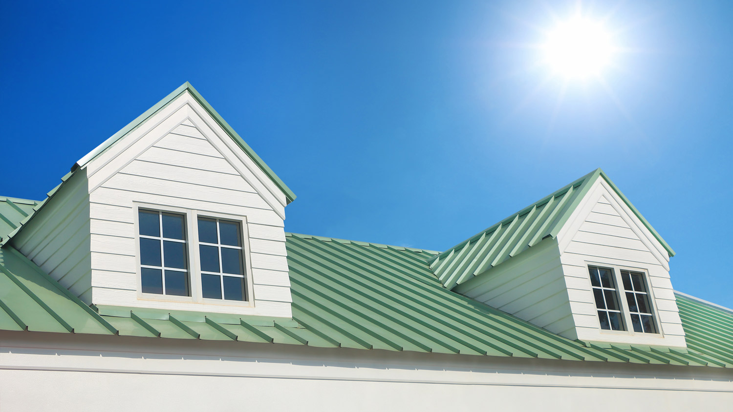 Dormer with windows on metal sheet roof with blue sky and sunshine