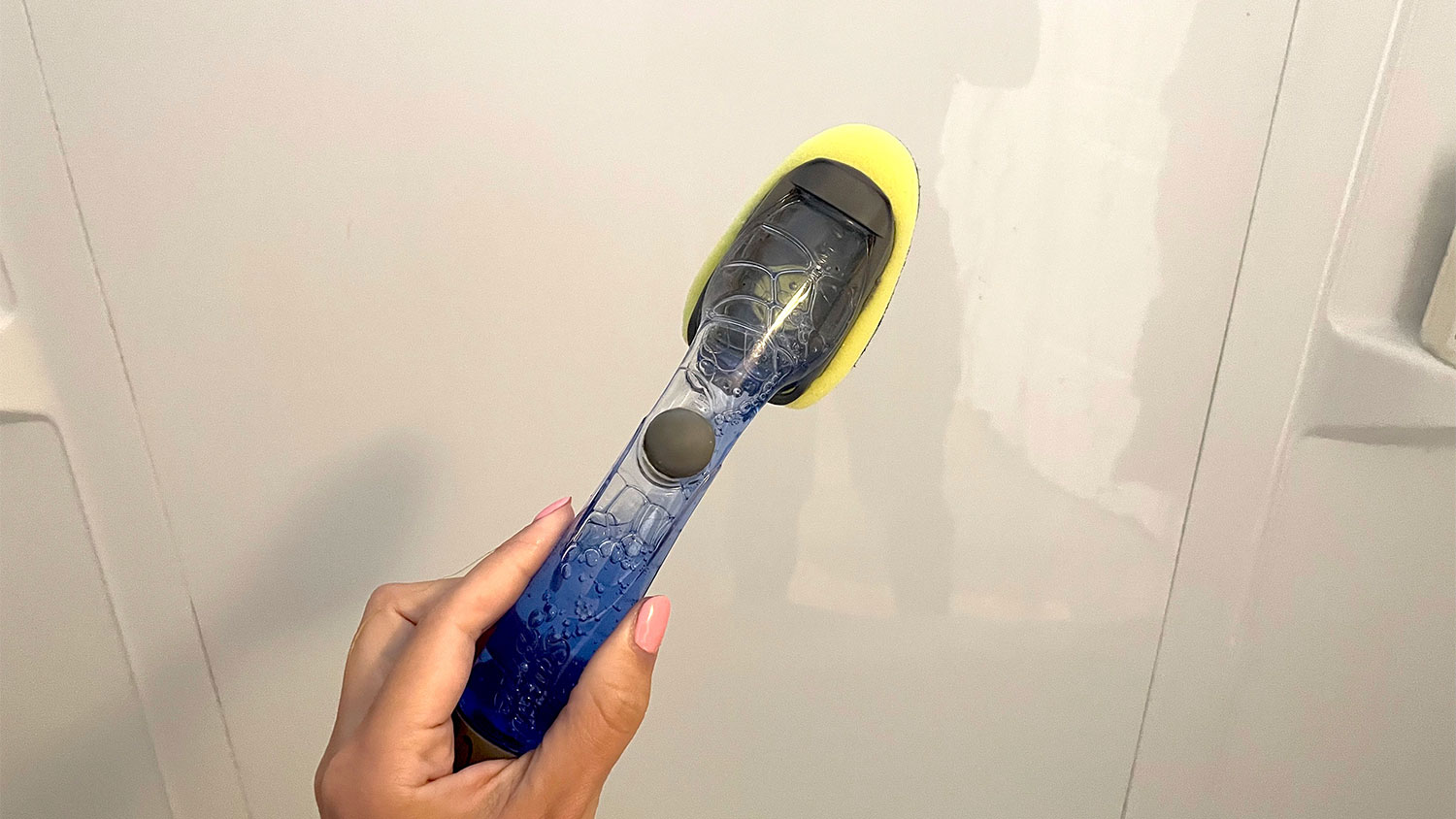 A woman holds a dish wand in front of a shower stall