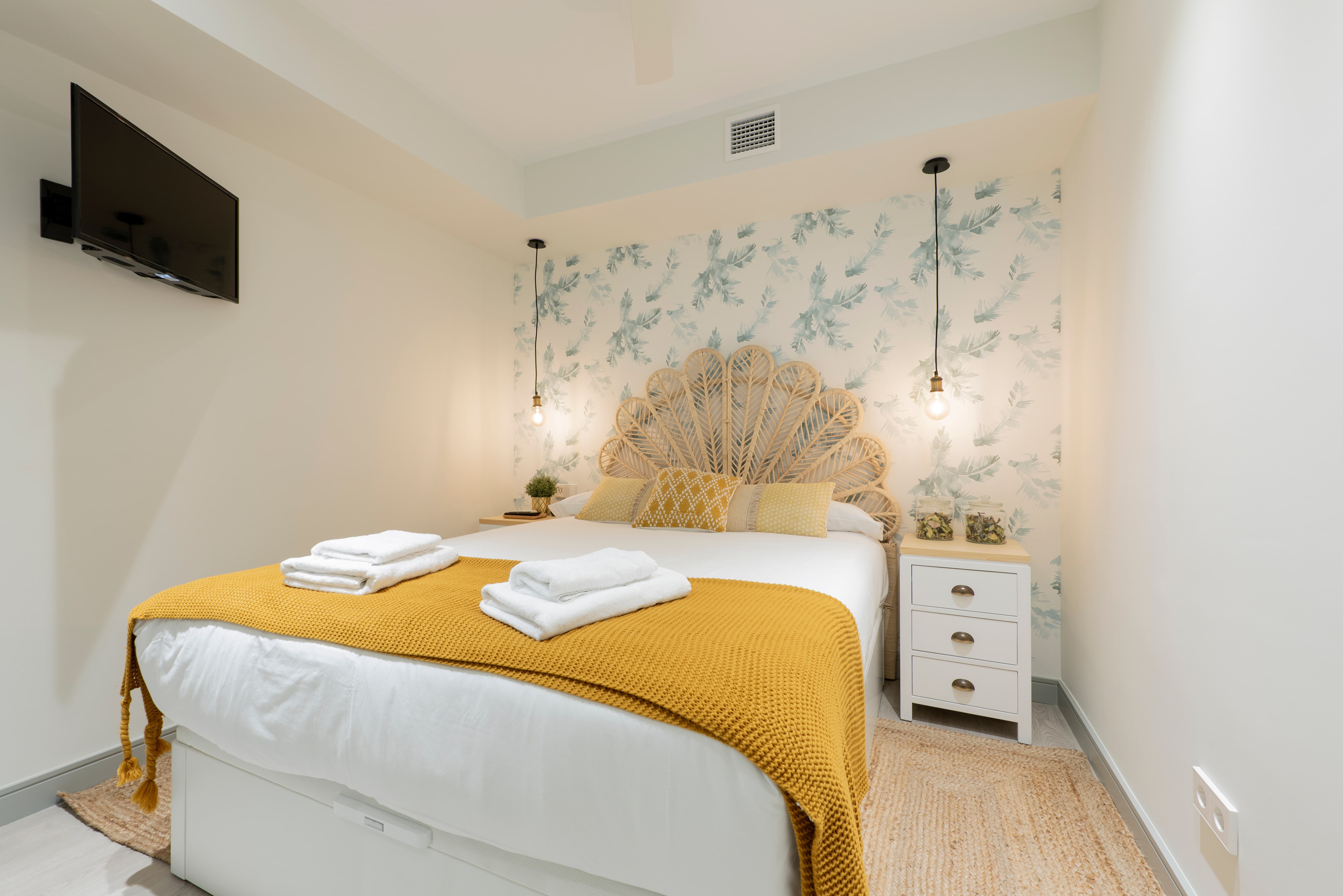 A small bedroom with one blue patterned accent wall and a rattan headboard