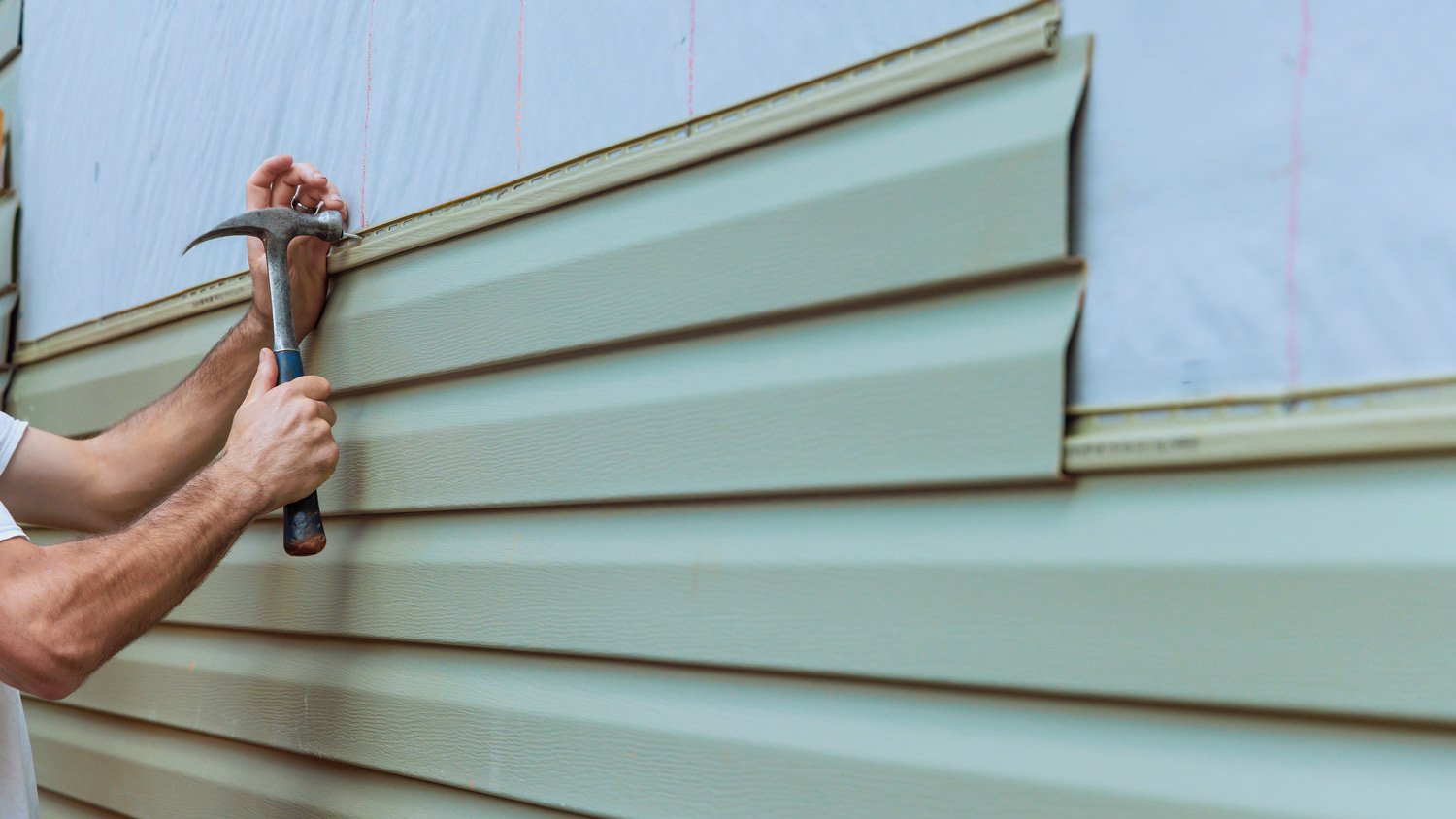 Contractor installing vinyl siding plastic panels on facade wall of new home