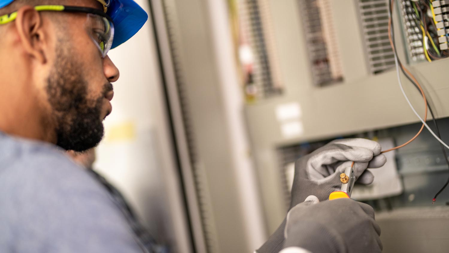 An electrician stripping a wire in front of a circuit breaker