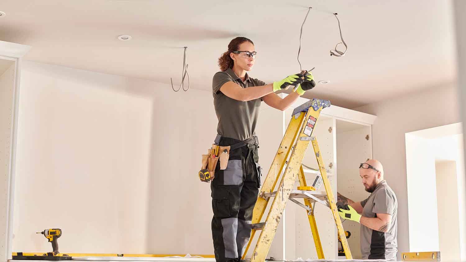  Female electrician on a ladder wiring a new kitchen