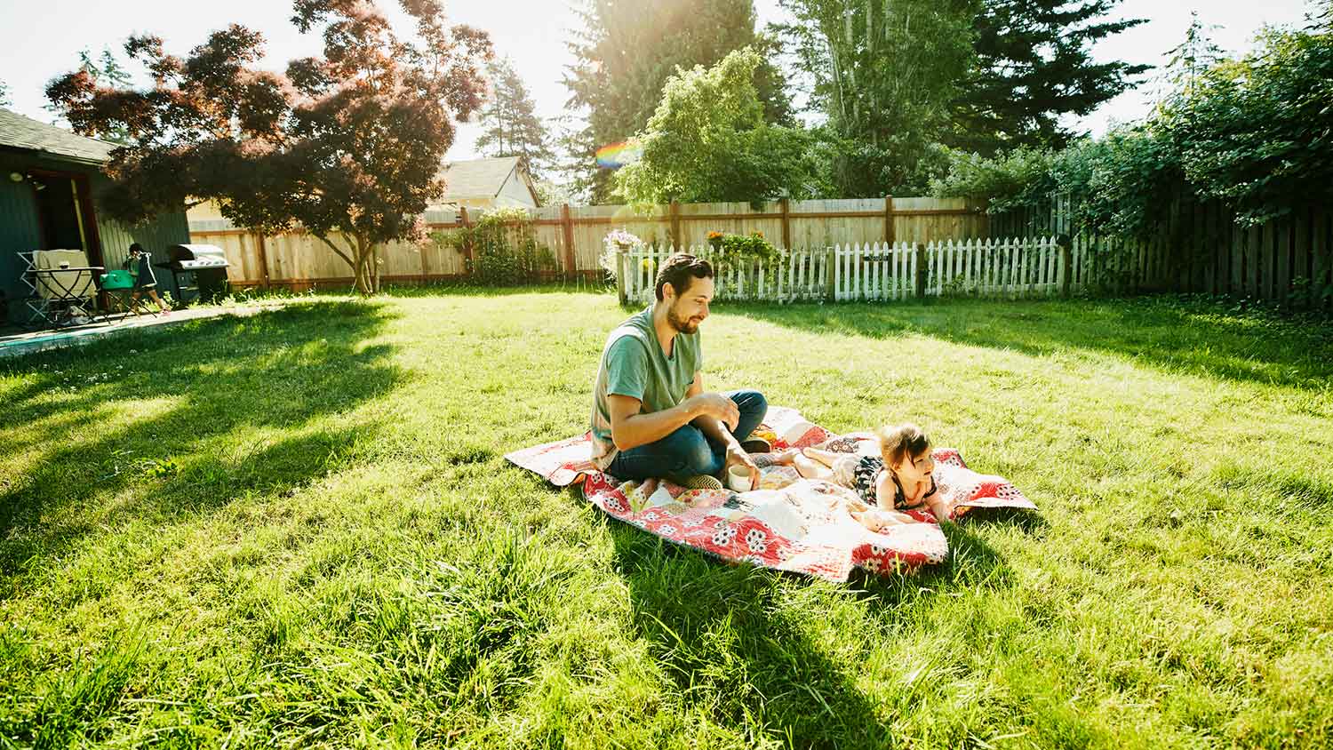 Father and daughter sitting on a blanket in the backyard