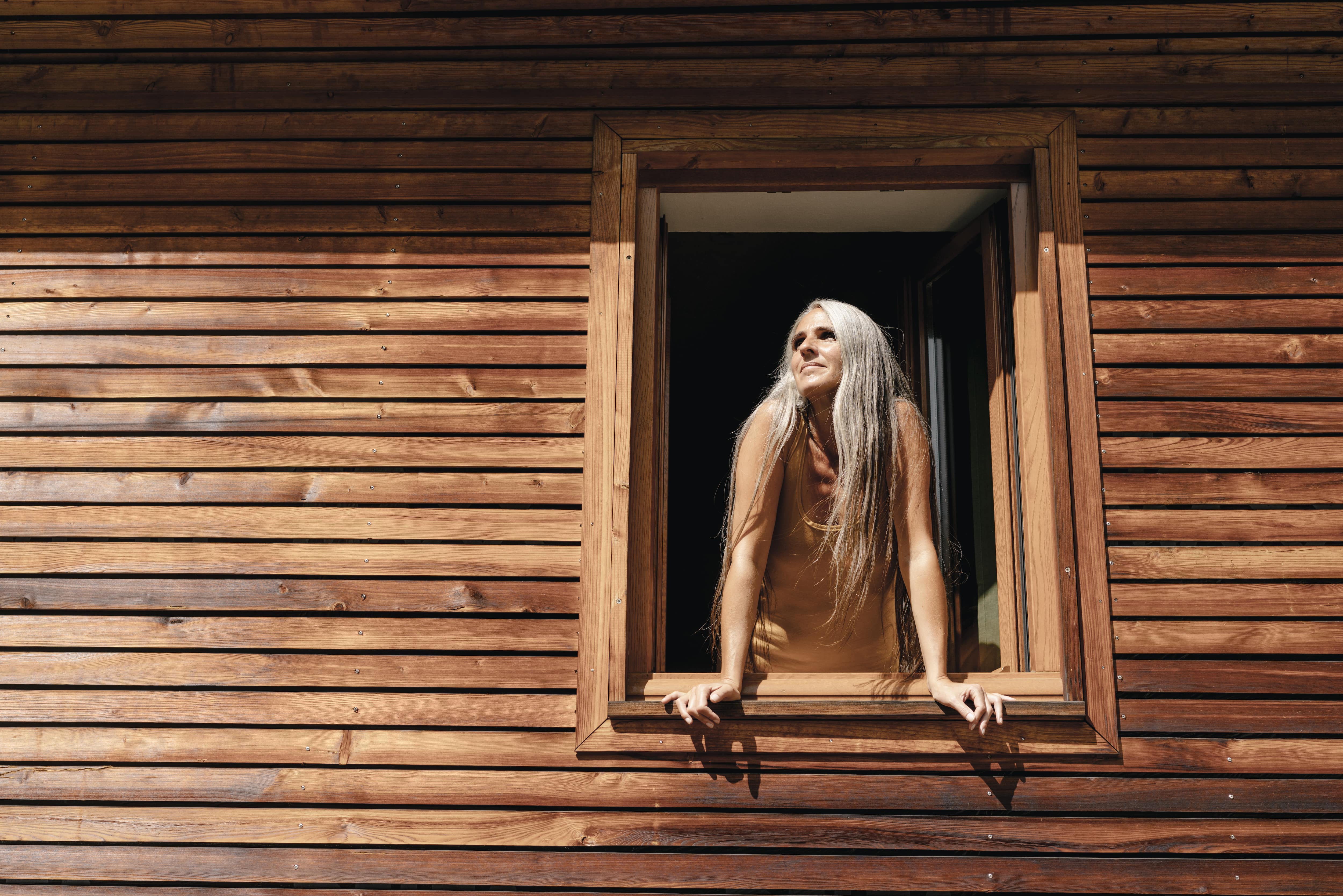 Woman looking out window with wooden trim and wooden exterior siding