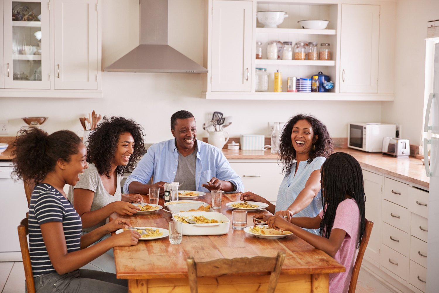 Family with teenage children eating a meal at a wooden table in a kitchen