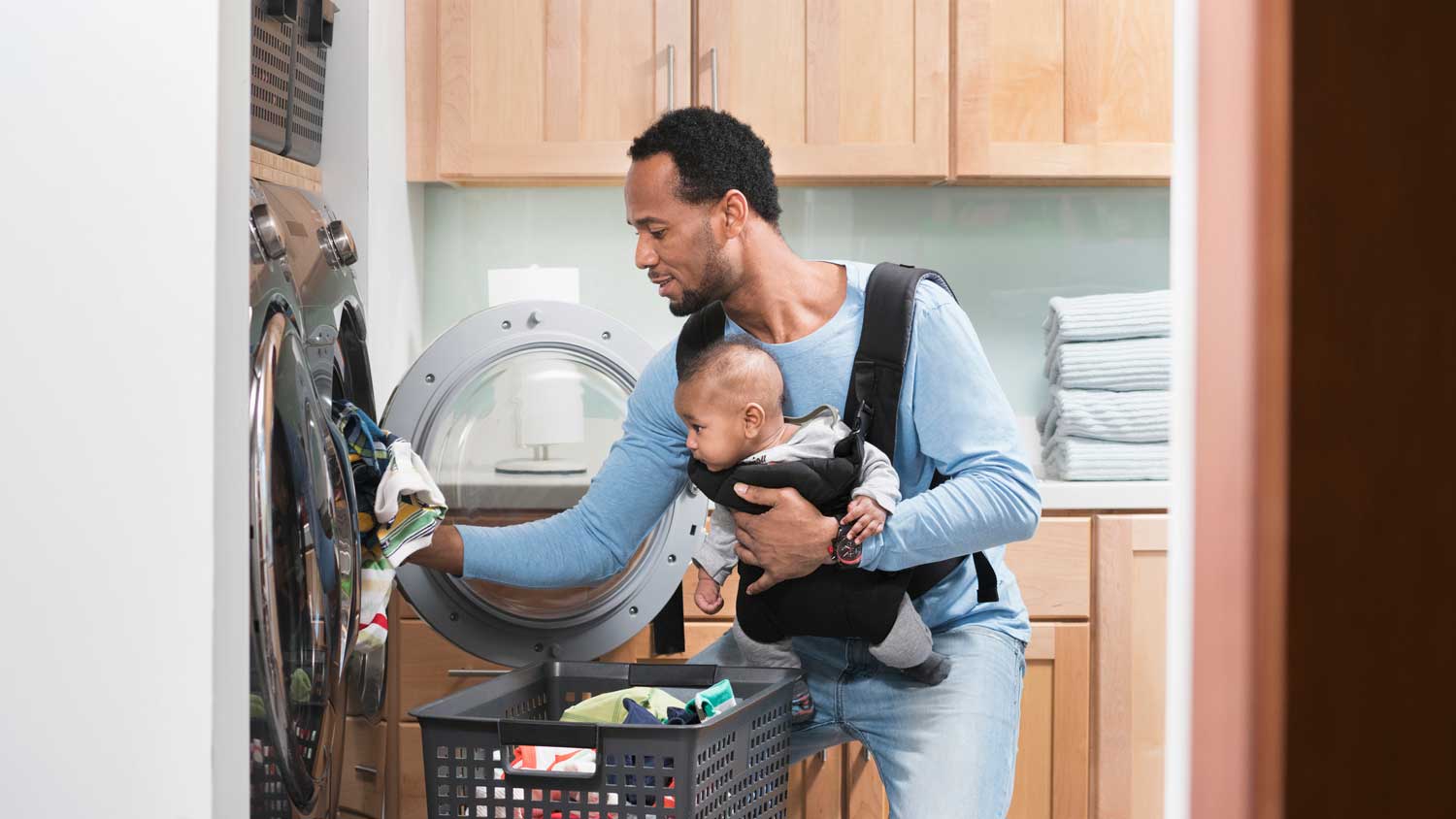 A father with his son in a baby carrier unloading clothes from dryer