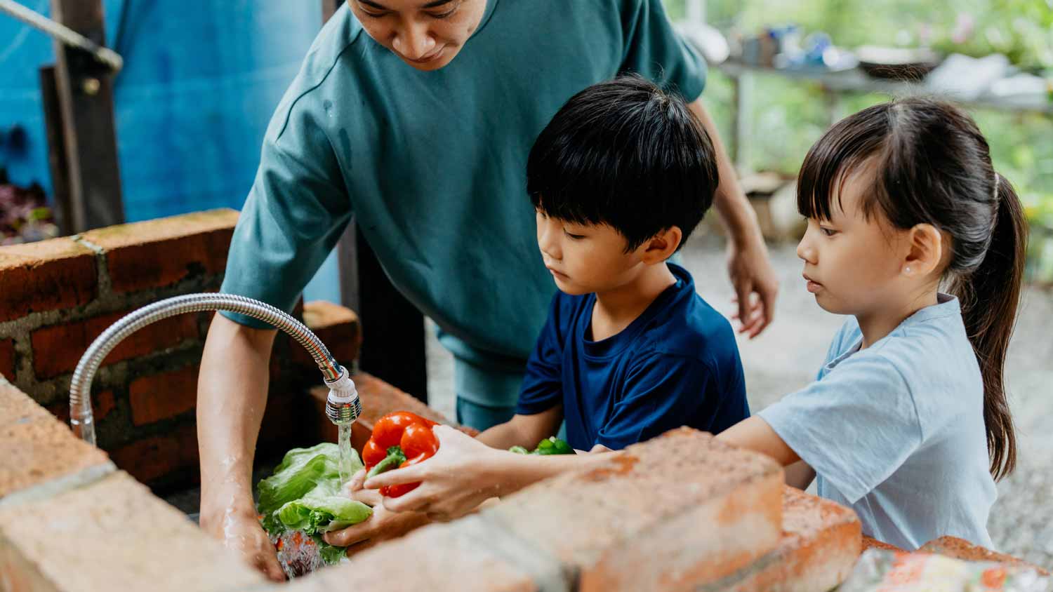 A father and his kids washing bell peppers in an outdoor sink