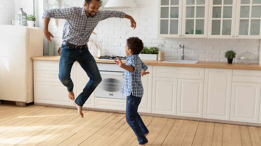 A father and his son dancing barefoot in the kitchen
