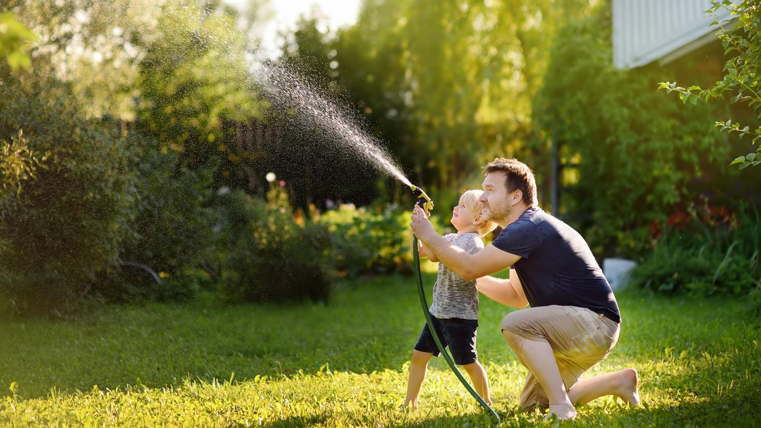 A father with his son watering the lawn with a hose