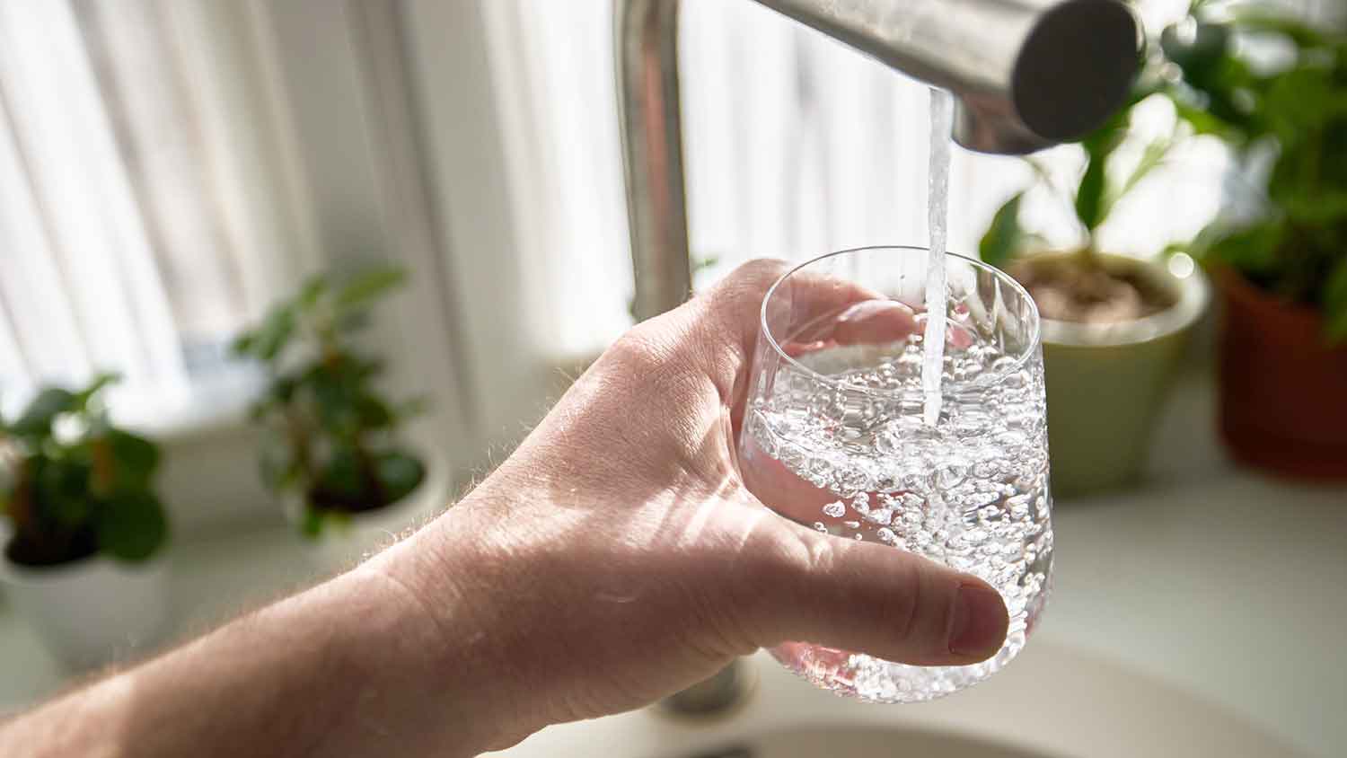 A hand holding a glass of bubbly water under the tap.