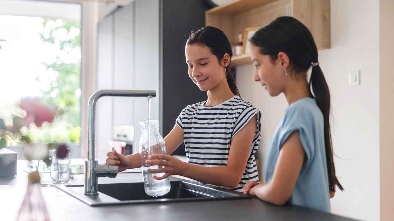 Two children fill a jar with clear water from the tap.