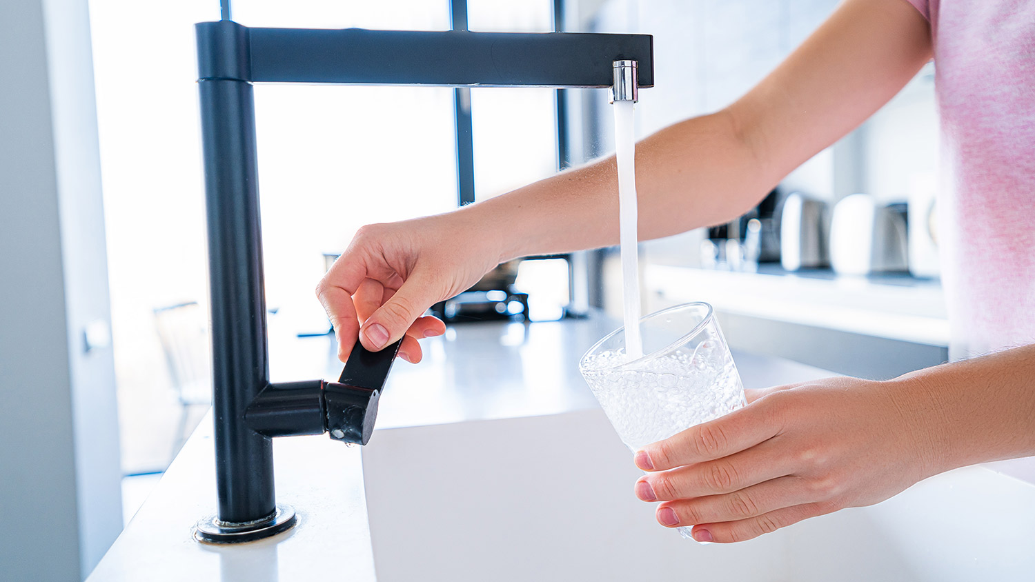 A woman fills a glass with water in the kitchen sink