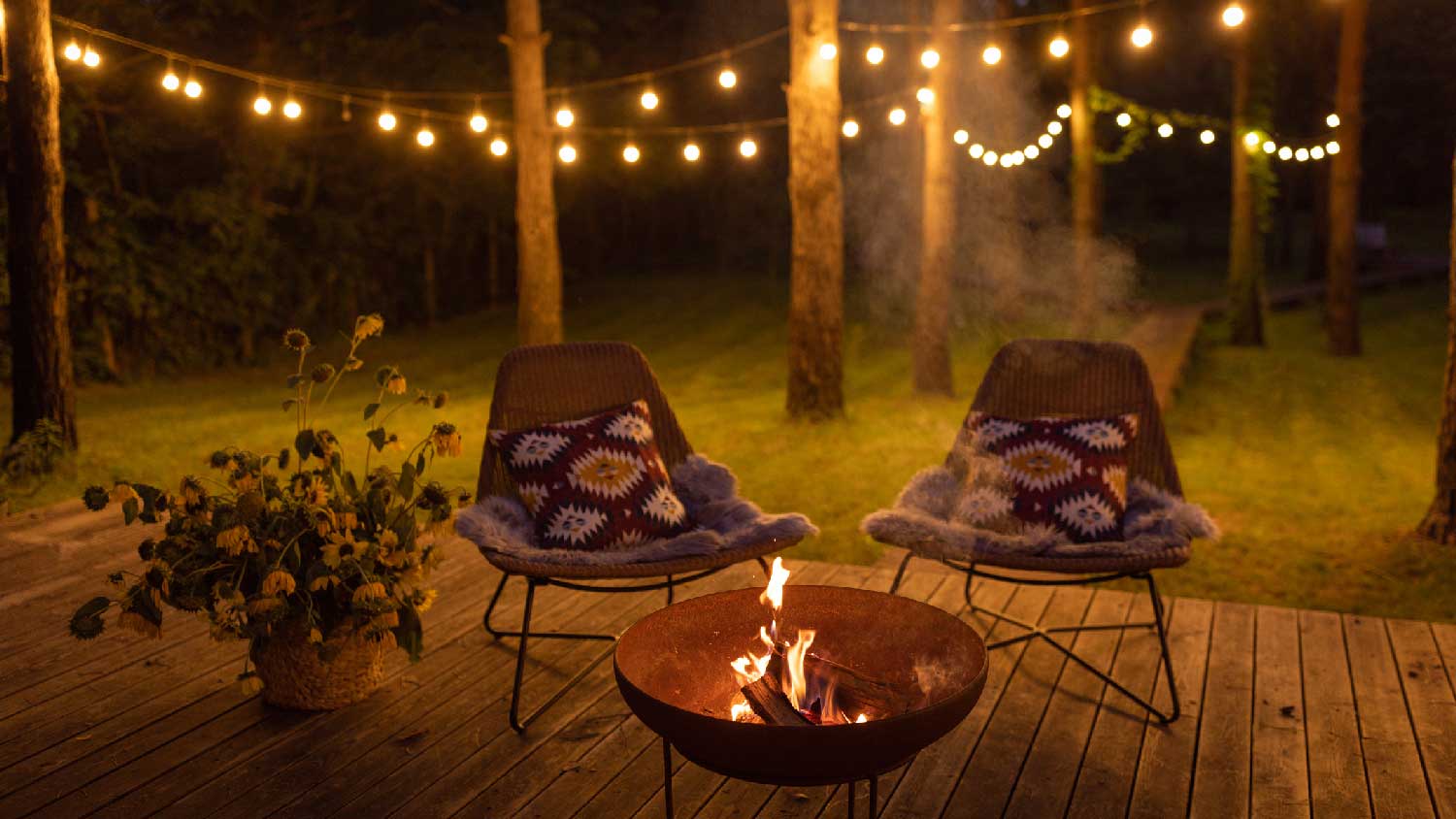 A fire pit with chairs and string lights in the background