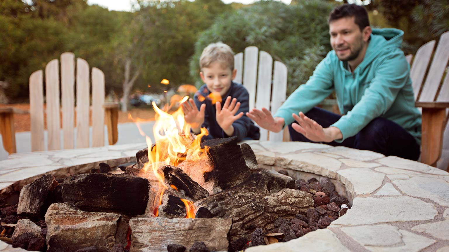 view of a firepit and happy smiling father and son warming their hands by the fire