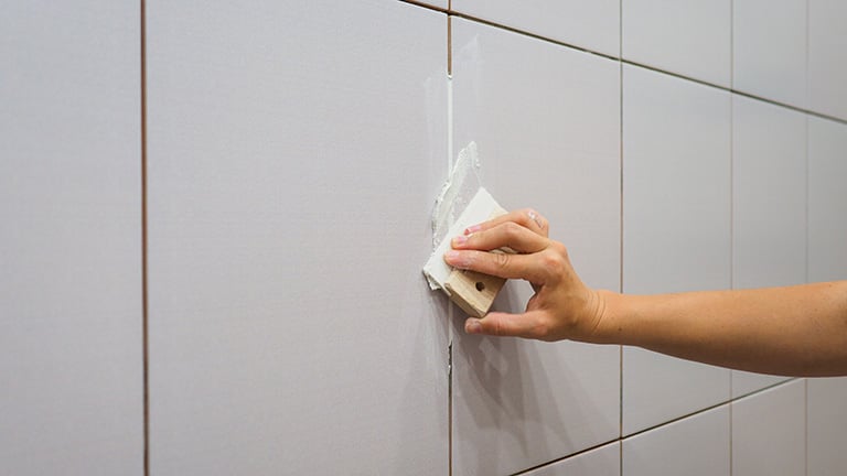 Detail of a woman’s hand fixing grout on bathroom tiles