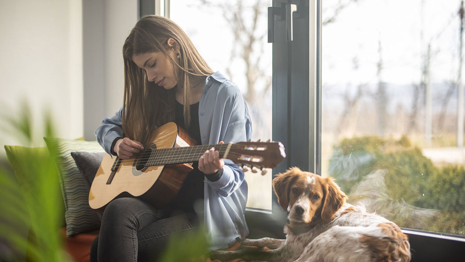 woman playing guitar with her dog by modern French doors