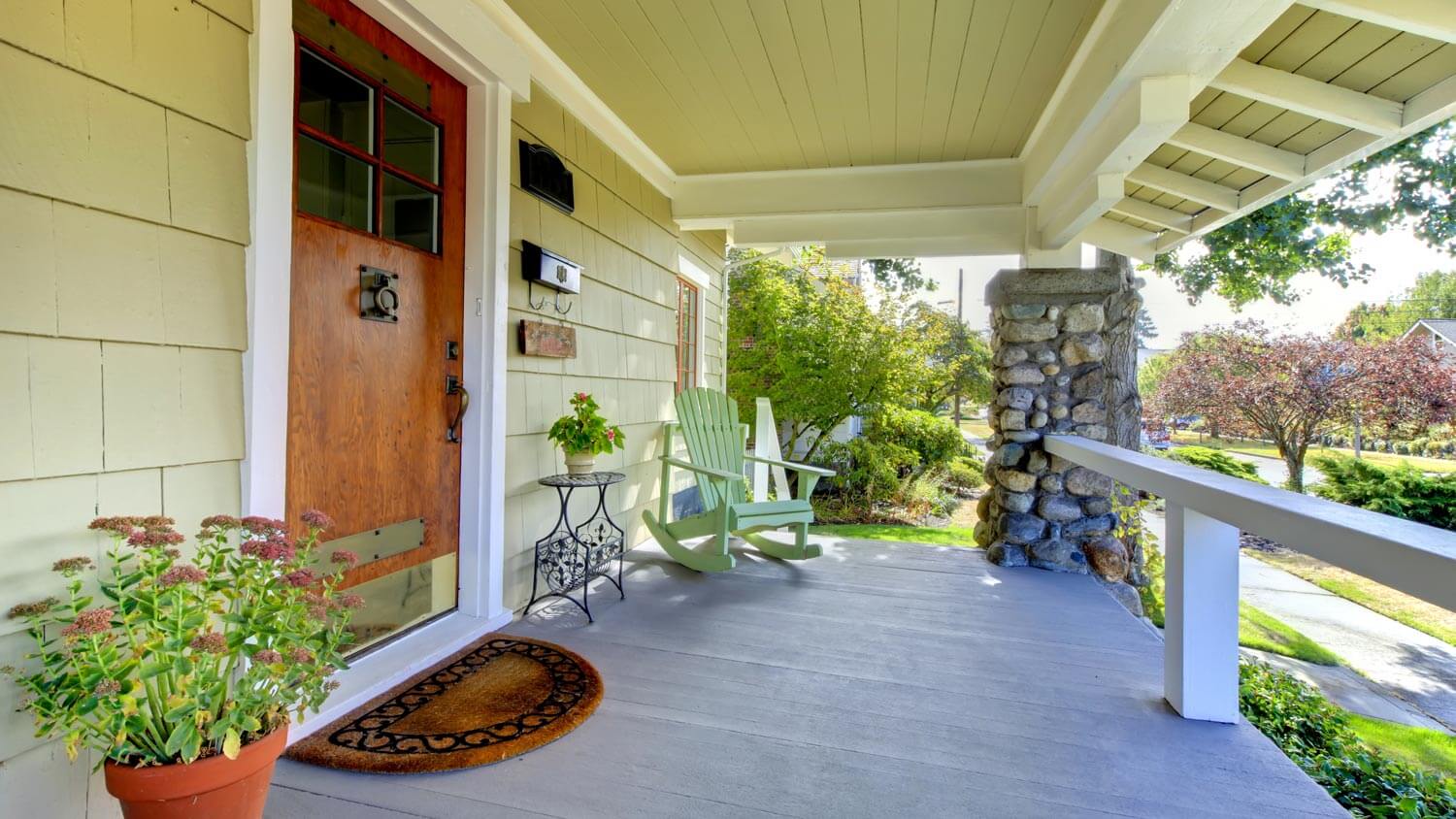 The front porch of a green and brown craftsman style house