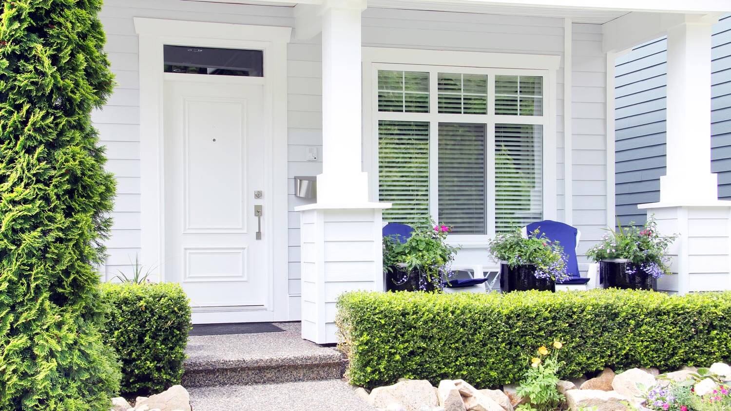 A white front porch with landscaped bushes