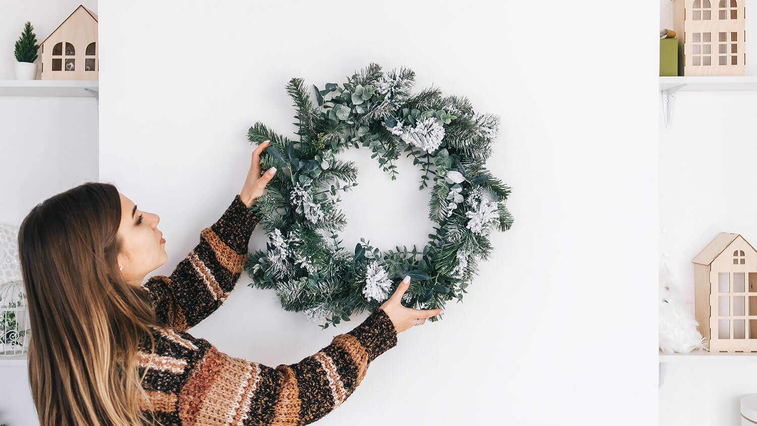 woman putting up a frosted forest wreath 