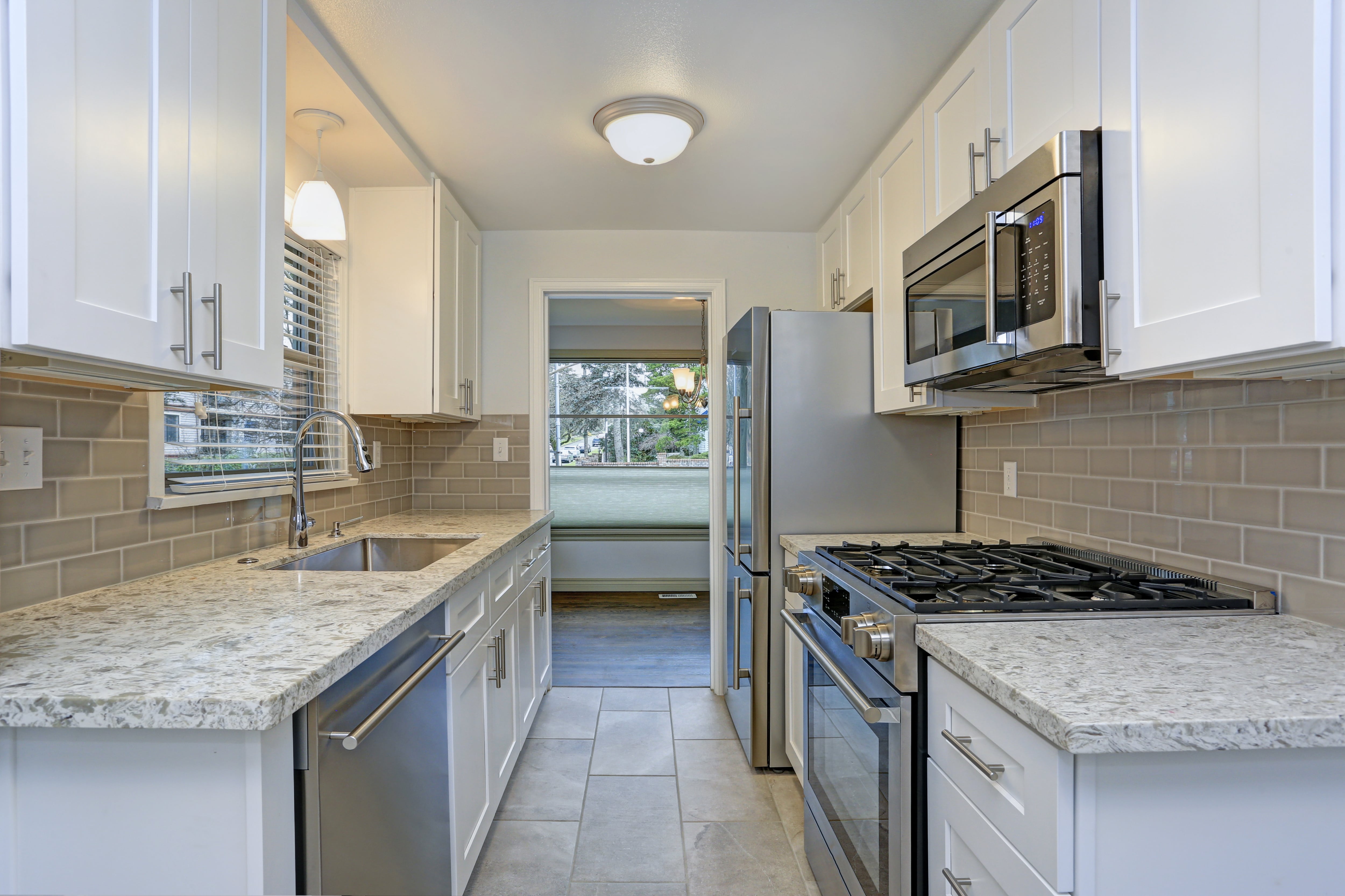 A small galley kitchen with white cabinets and gray subway tile