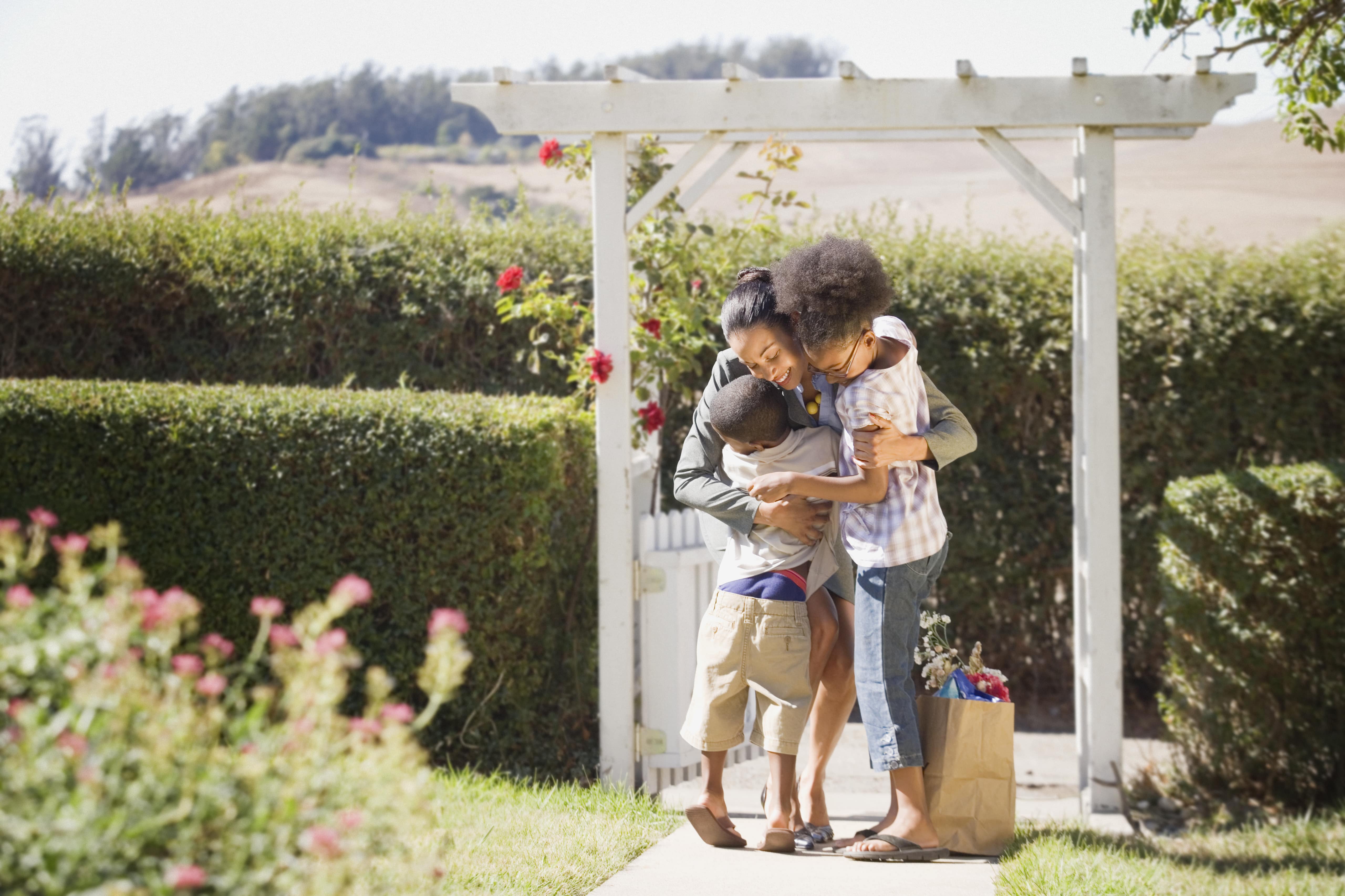 Woman hugging children under white garden arbor