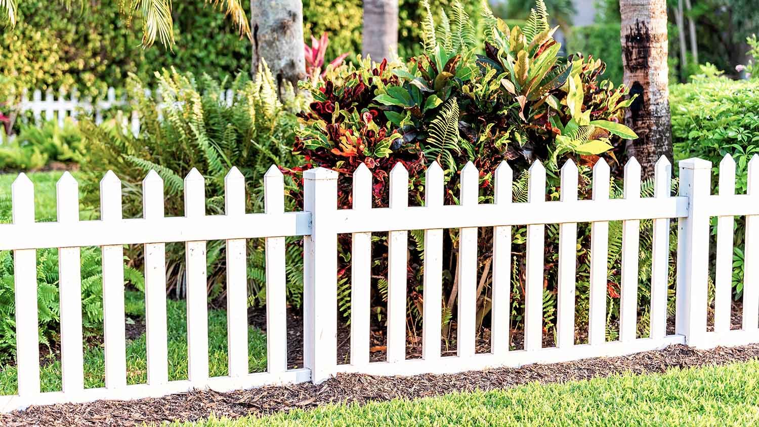 A view of a garden through a white fence