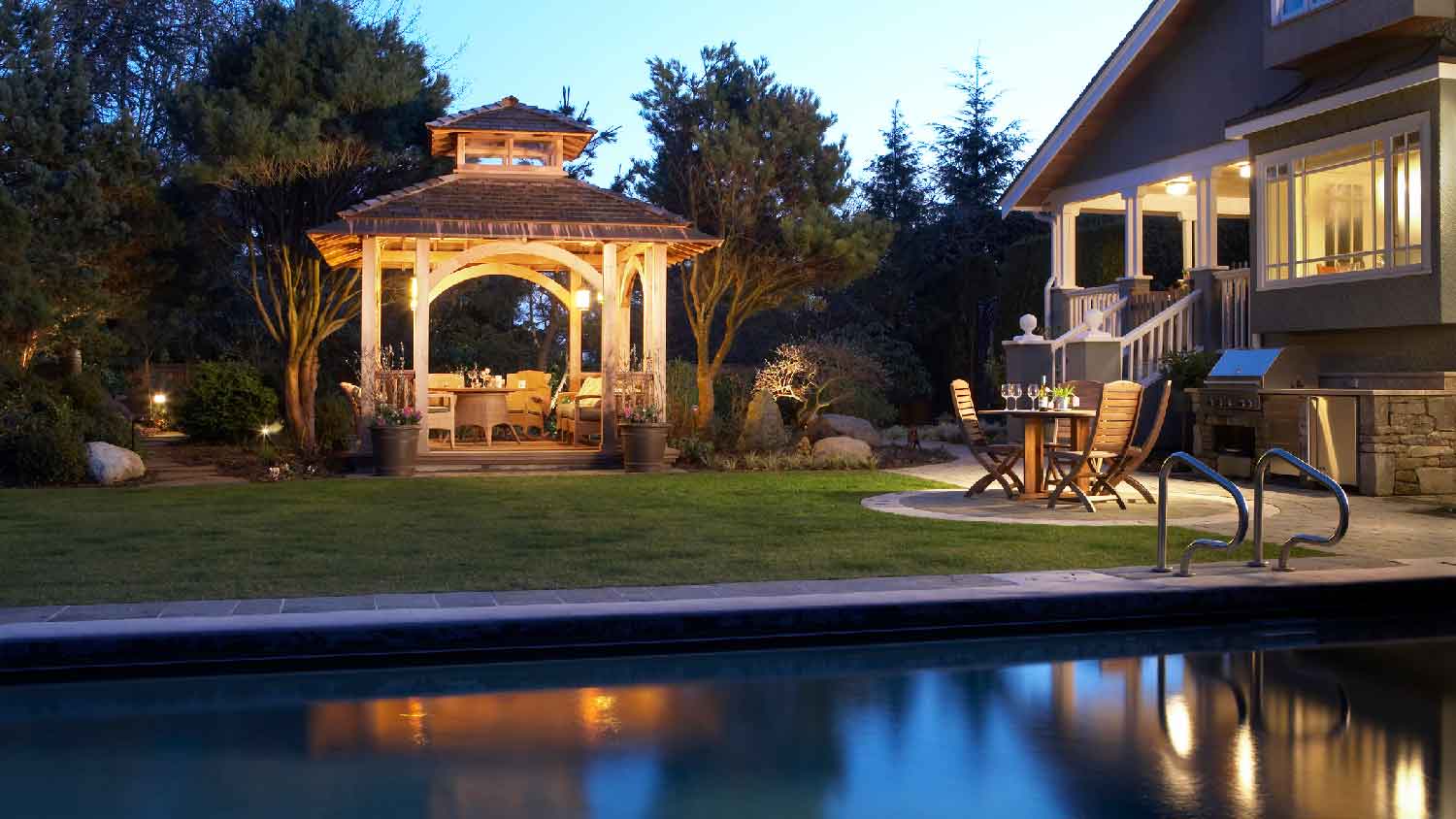 A gazebo and a pool at dusk illuminated by external light