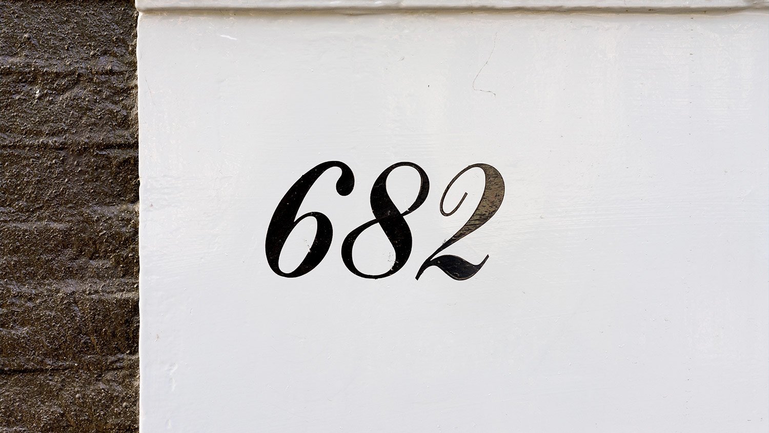 black house number (682) painted on white concrete 