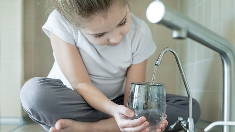 Young girl getting water from sink