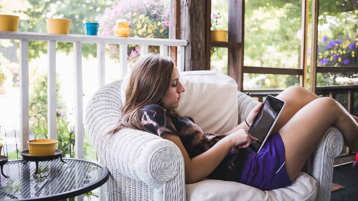 A girl relaxing with her tablet in a screened-in porch