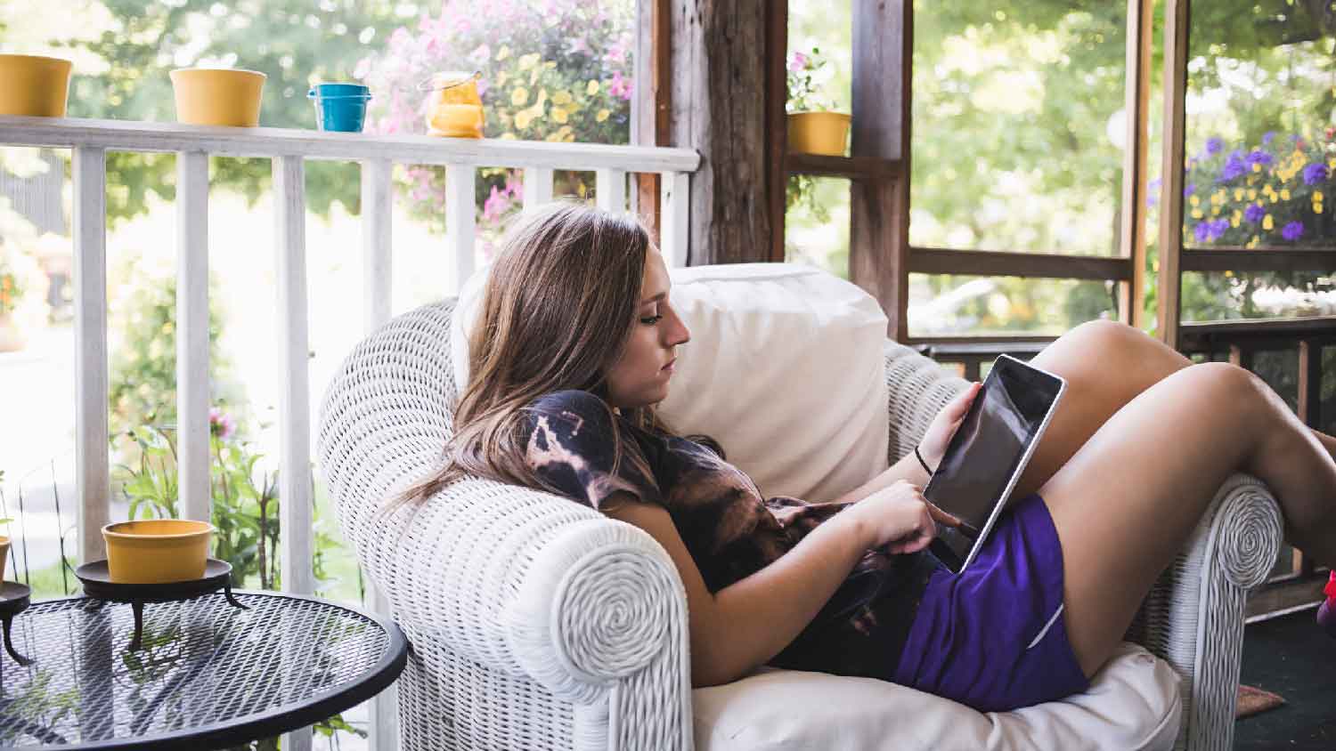 A girl relaxing with her tablet in a screened-in porch 