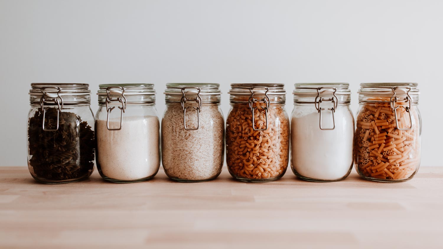 Six glass jars full with dried uncooked food ingredients