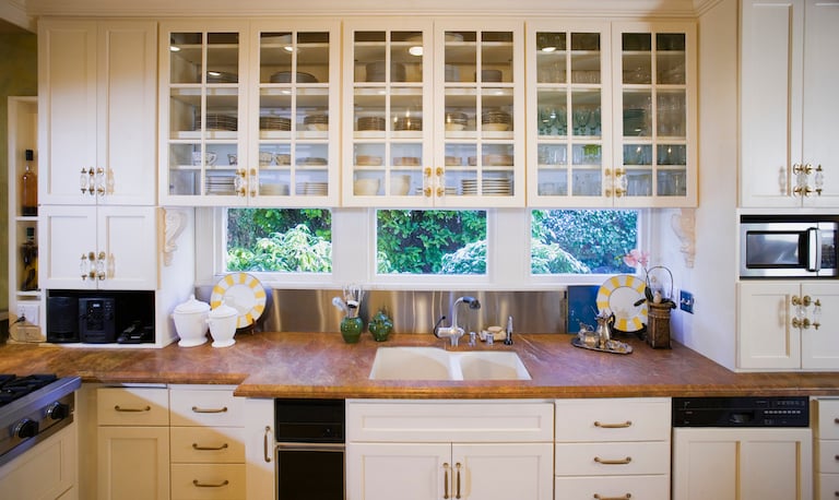 kitchen with windows, wood countertop, and cream cabinets with glass