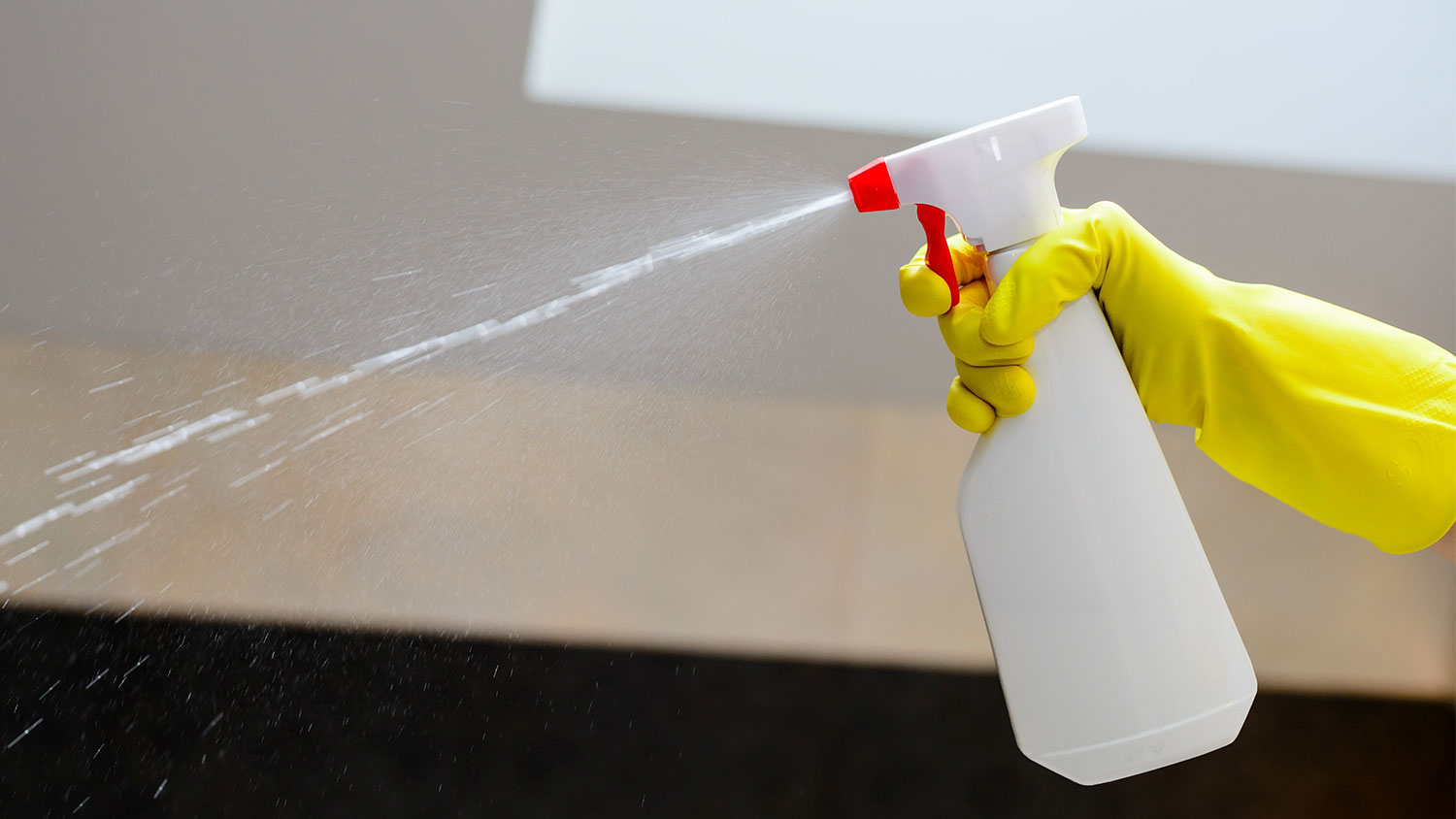 A gloved hand sprays a spray bottle